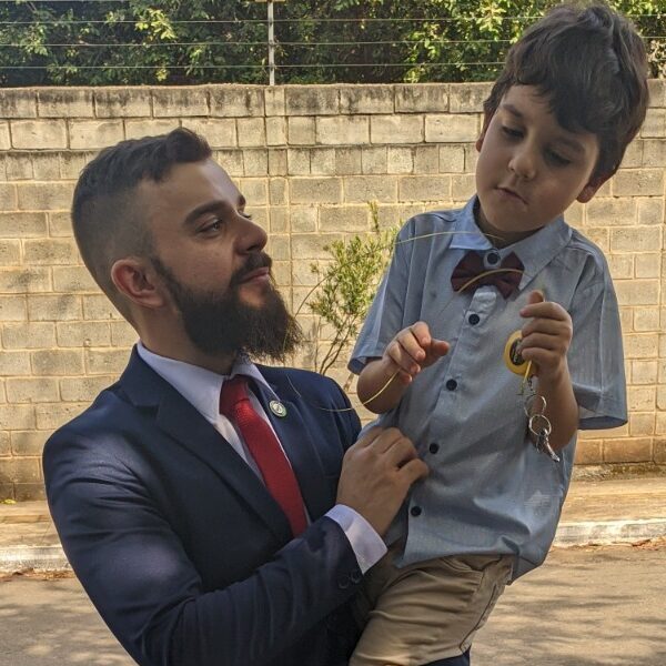 Advogado de terno segurando o filho caçula autista no colo em ambiente externo, representando cuidado, responsabilidade e compromisso com o direito à saúde
