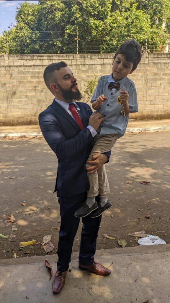 Advogado de terno segurando o filho caçula autista no colo em ambiente externo, representando cuidado, responsabilidade e compromisso com o direito à saúde